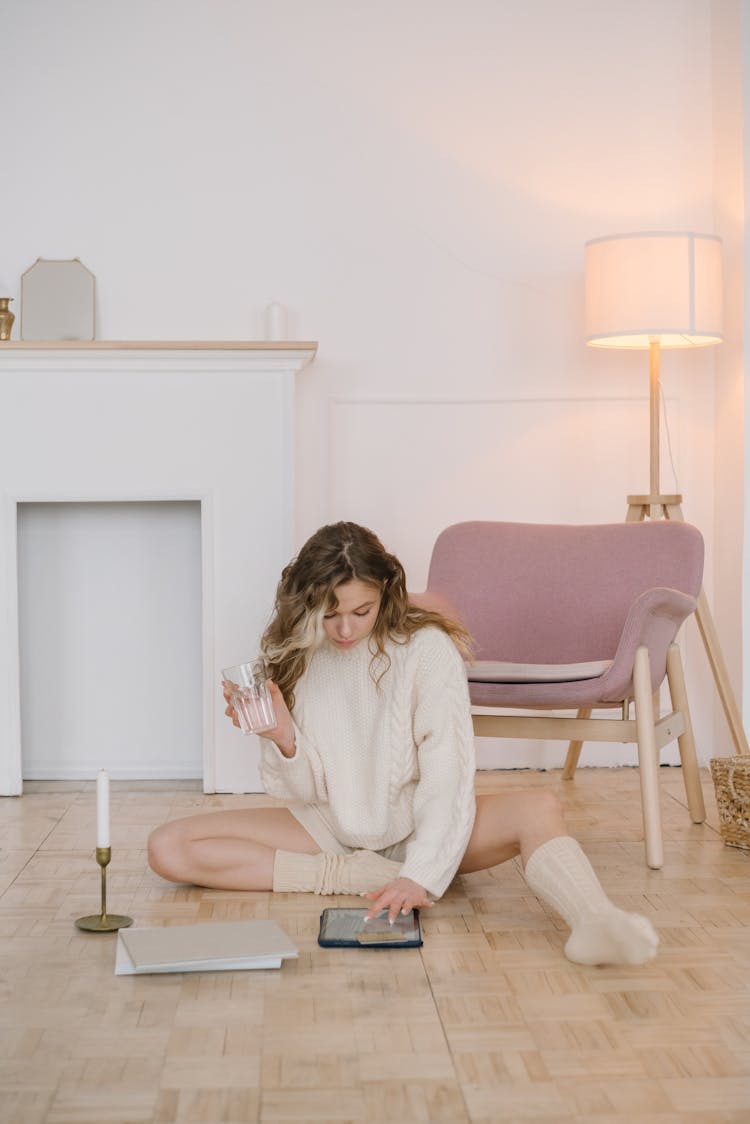 Woman In White Sweater Sitting On A Wooden Floor Using An IPad