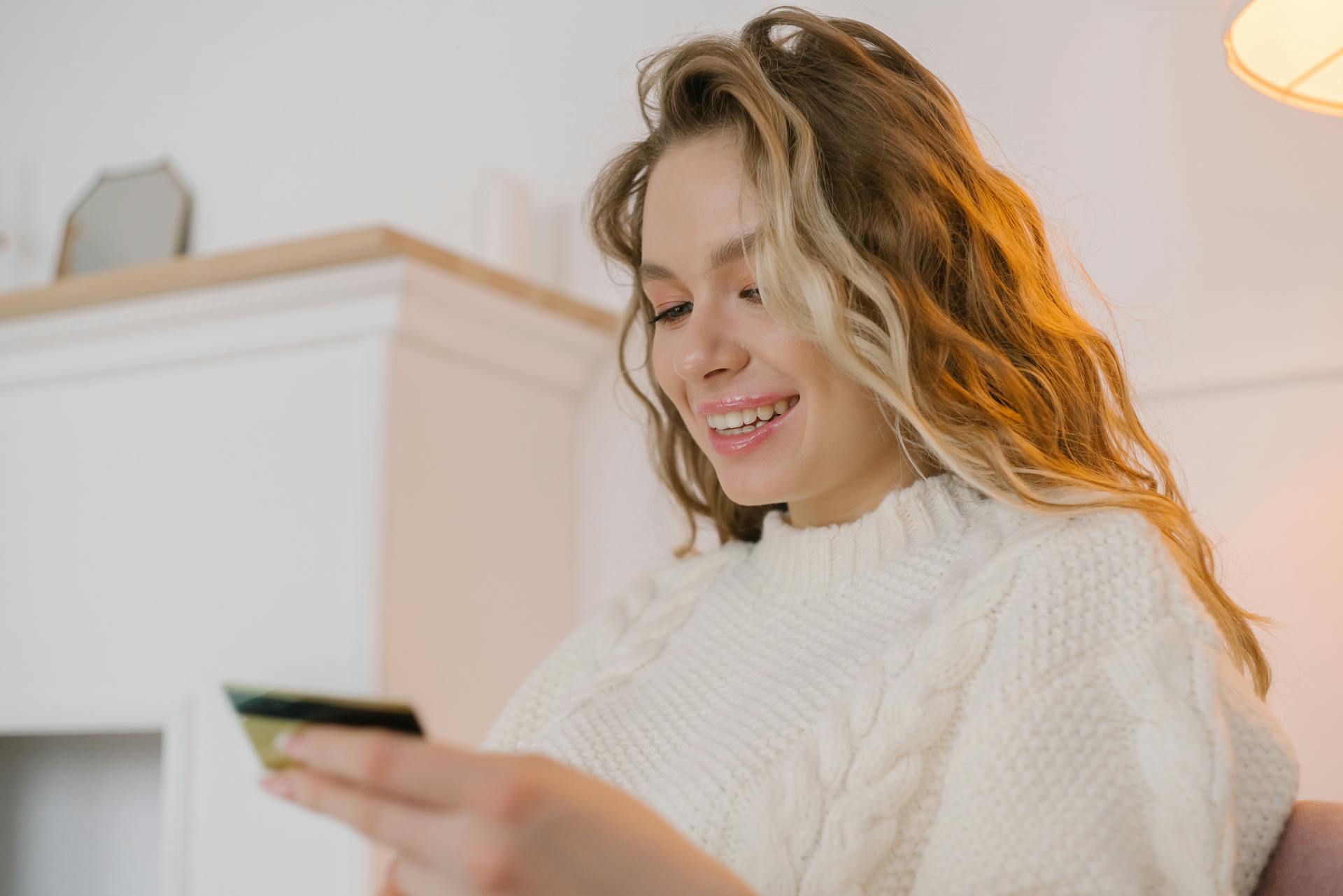 Happy woman holding a credit card shopping online from home in a cozy sweater.