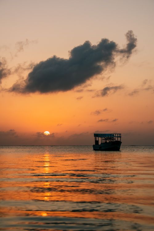Free A tranquil sunset view with a solitary boat on the calm sea, ideal for travel and relaxation themes. Stock Photo