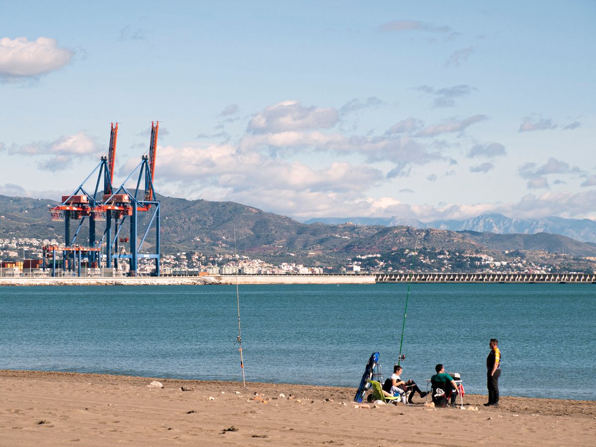 Málaga - pescari pe o plajă cu macaralele portului în fundal