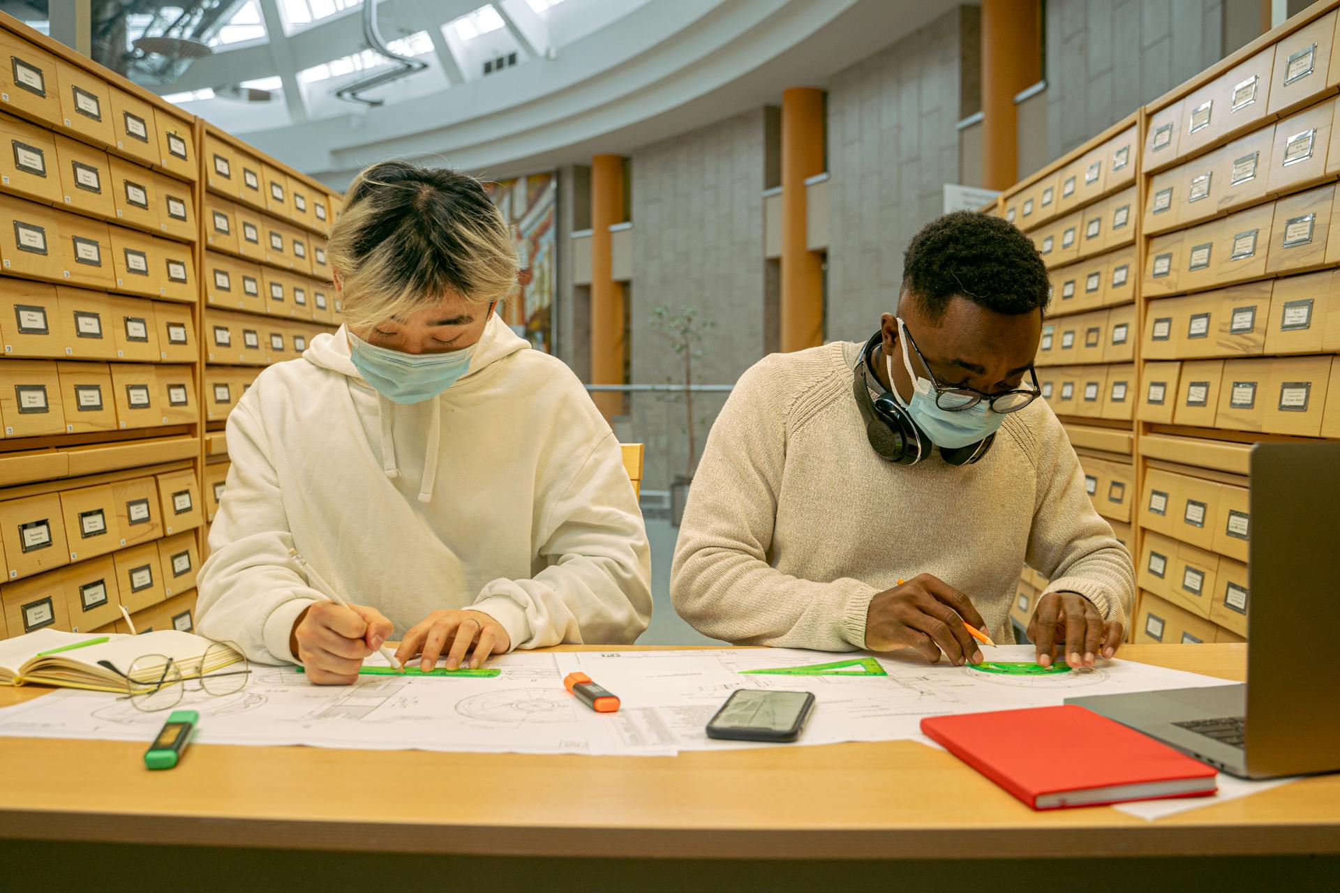 Two students studying carefully in library, following new normal safety guidelines.