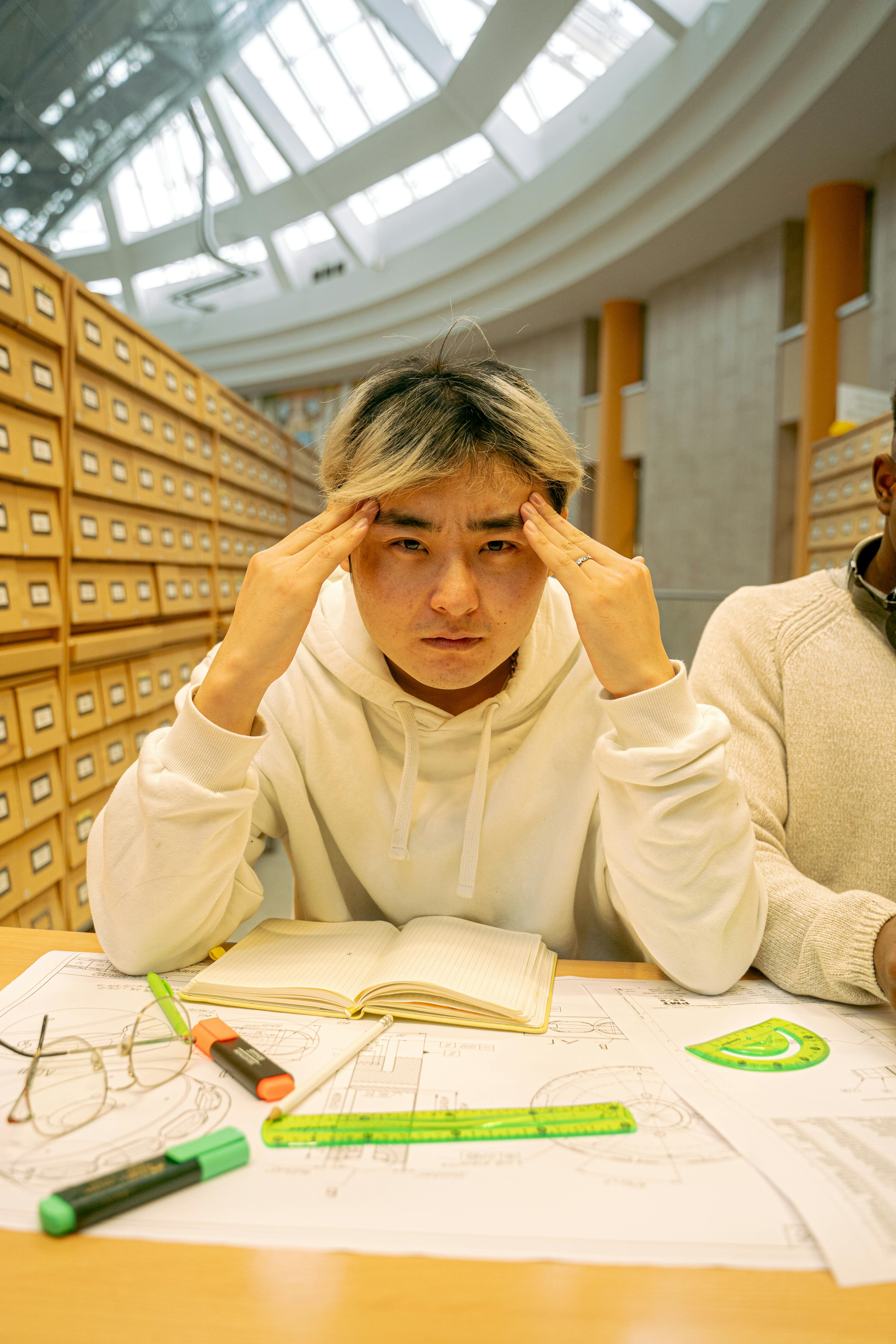 Asian student concentrating on study materials inside a modern library setting.