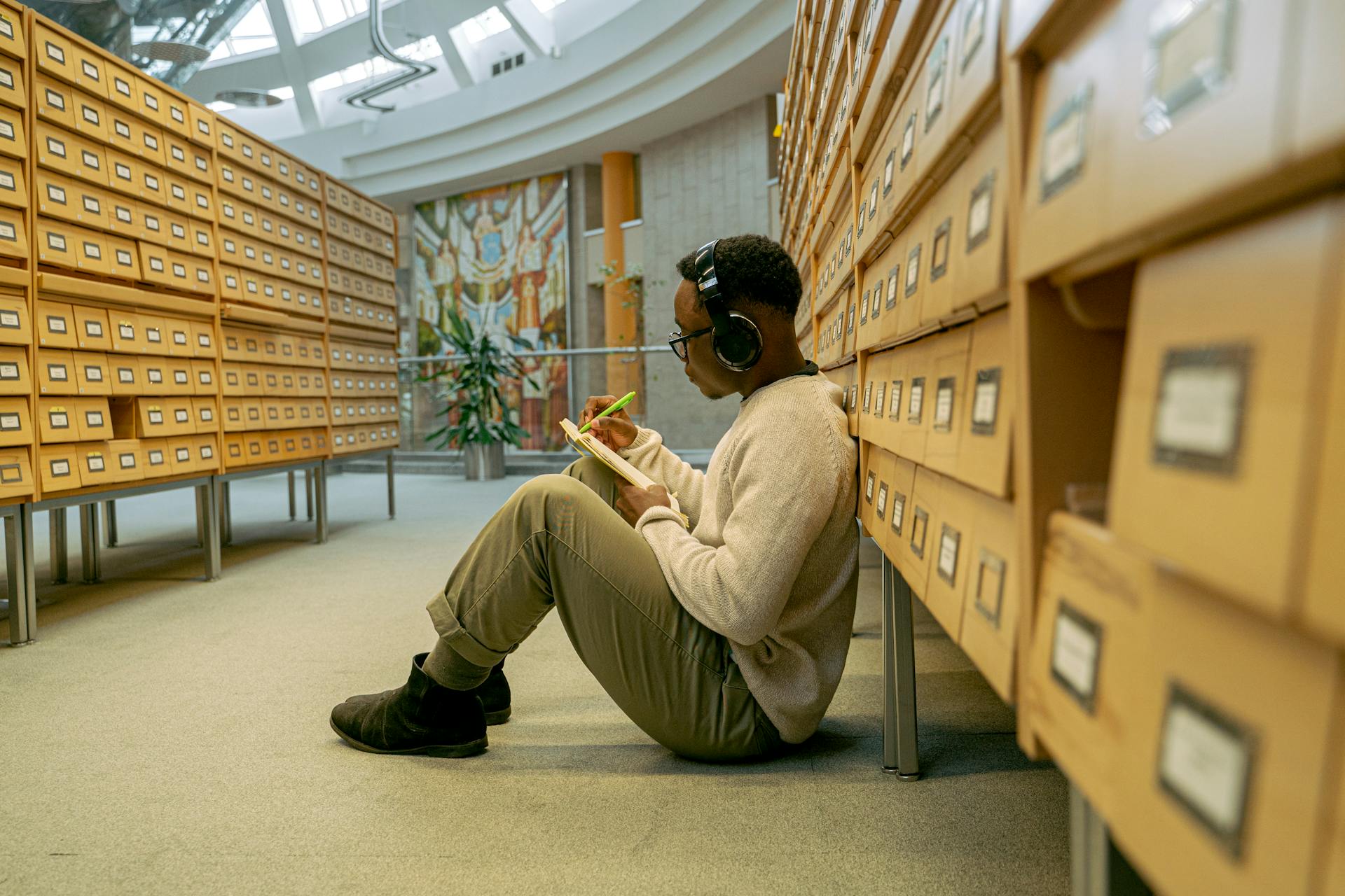 African American man sitting indoors with headphones, writing notes while listening to music