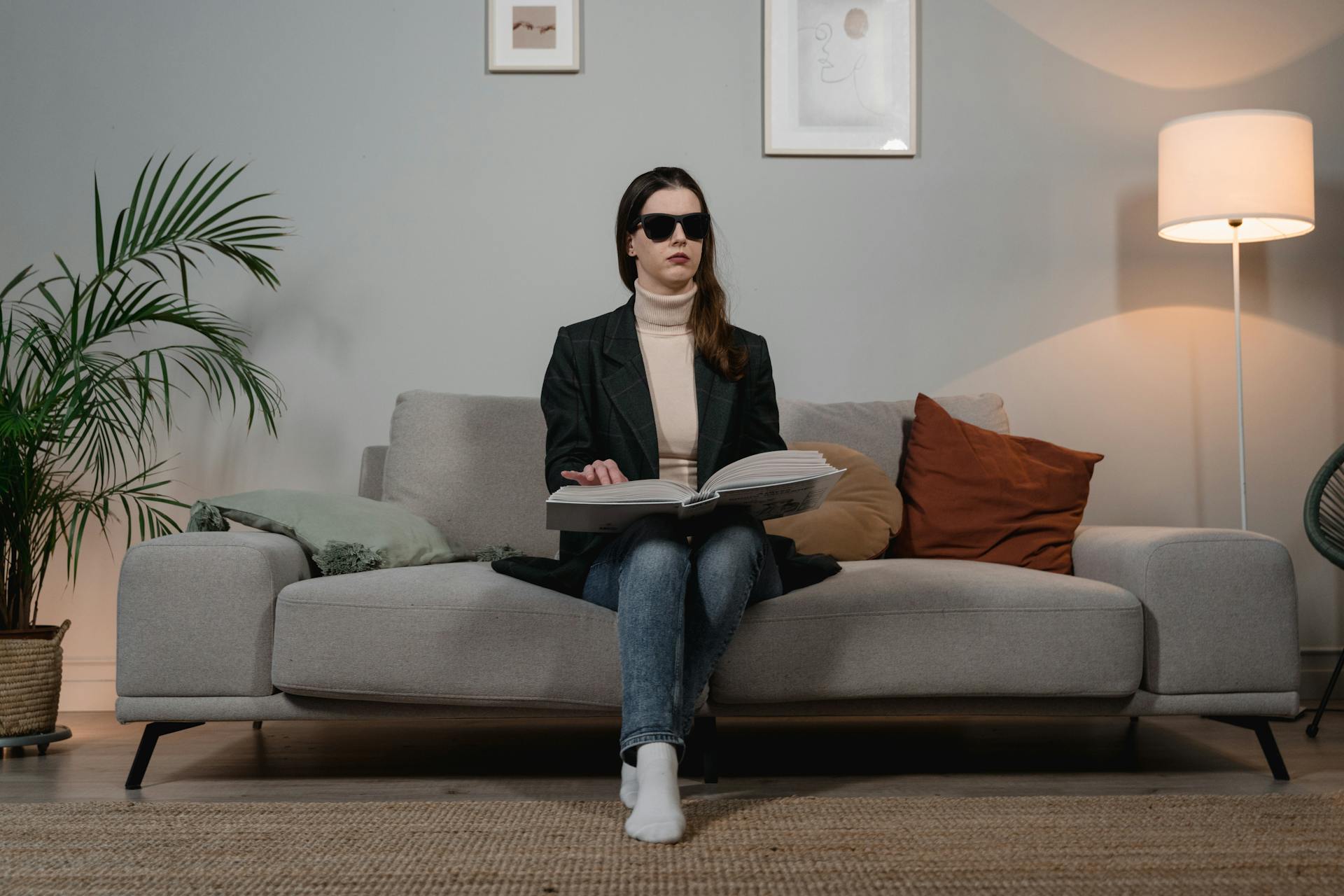 Woman with disability reading Braille book on a sofa indoors.