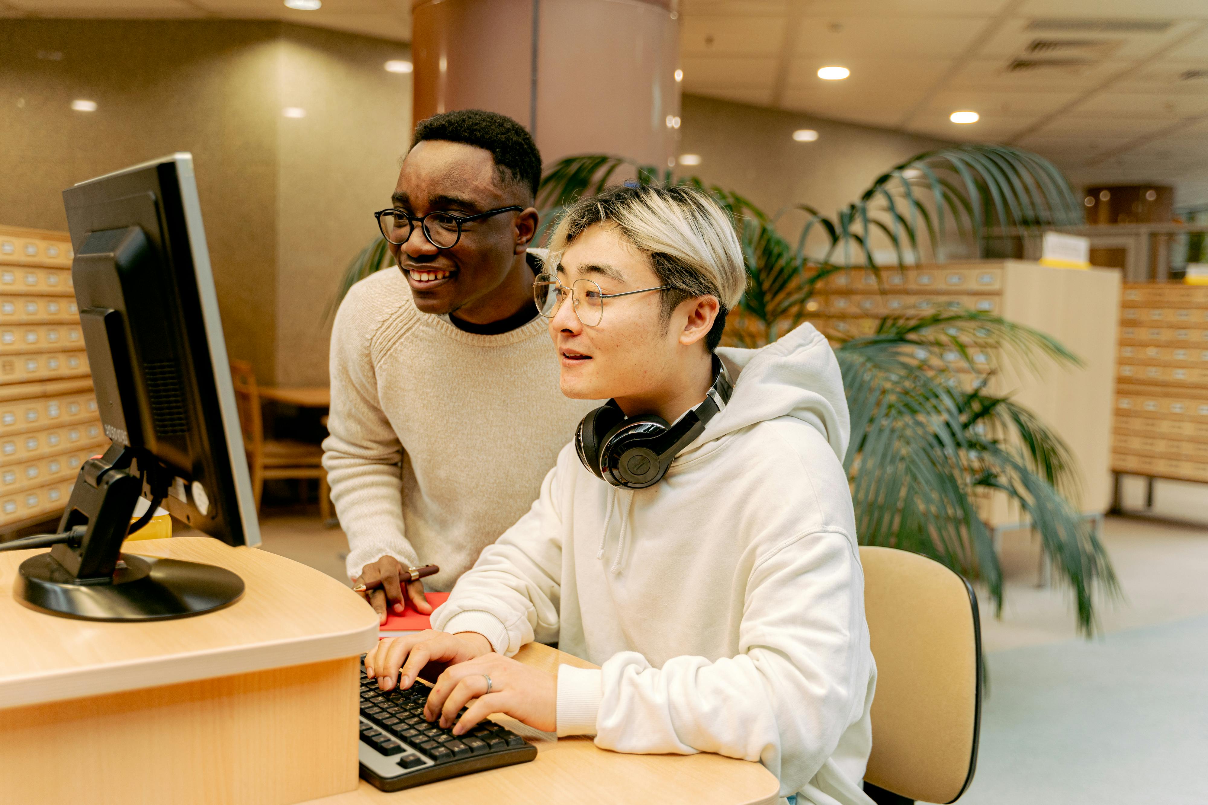 Two students collaborating on a computer in a library setting, focused on their studies.