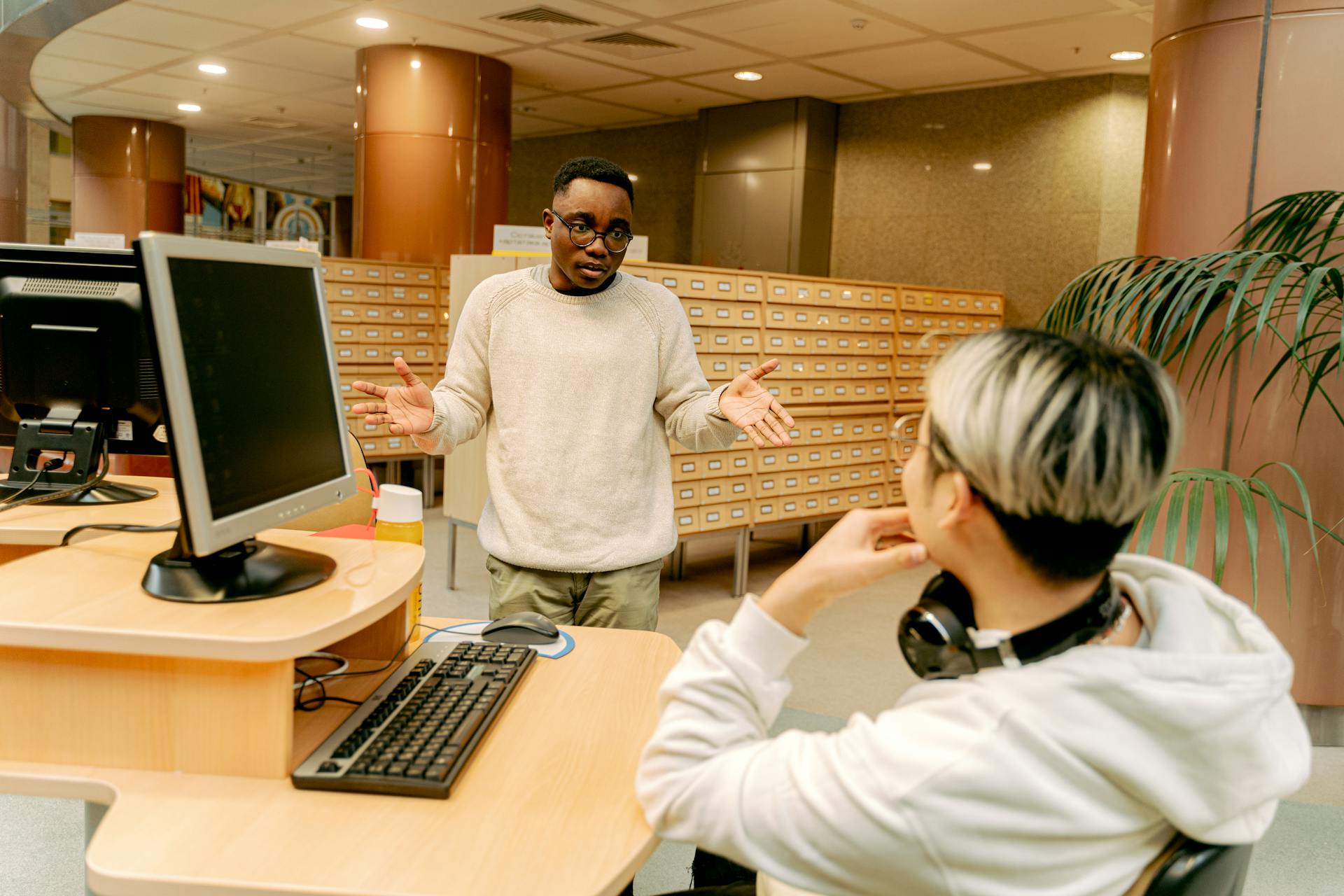 Two students engage in a discussion at a university library, focusing on a technology project.