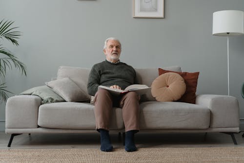 Elderly Man Sitting on Sofa While Holding a Book