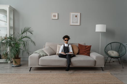 A young girl with visual impairment sits on a couch reading braille, showcasing inclusivity.