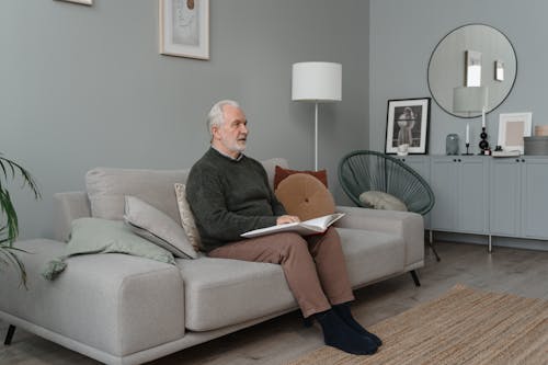 Elderly Man Sitting on Gray Couch Reading a Book Using Braille