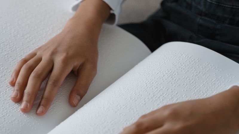 Close-up of a child's hands reading a book in braille at a classroom table