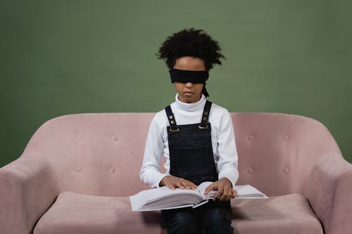 A Girl Sitting on the Couch Blindfolded while Touching the Book