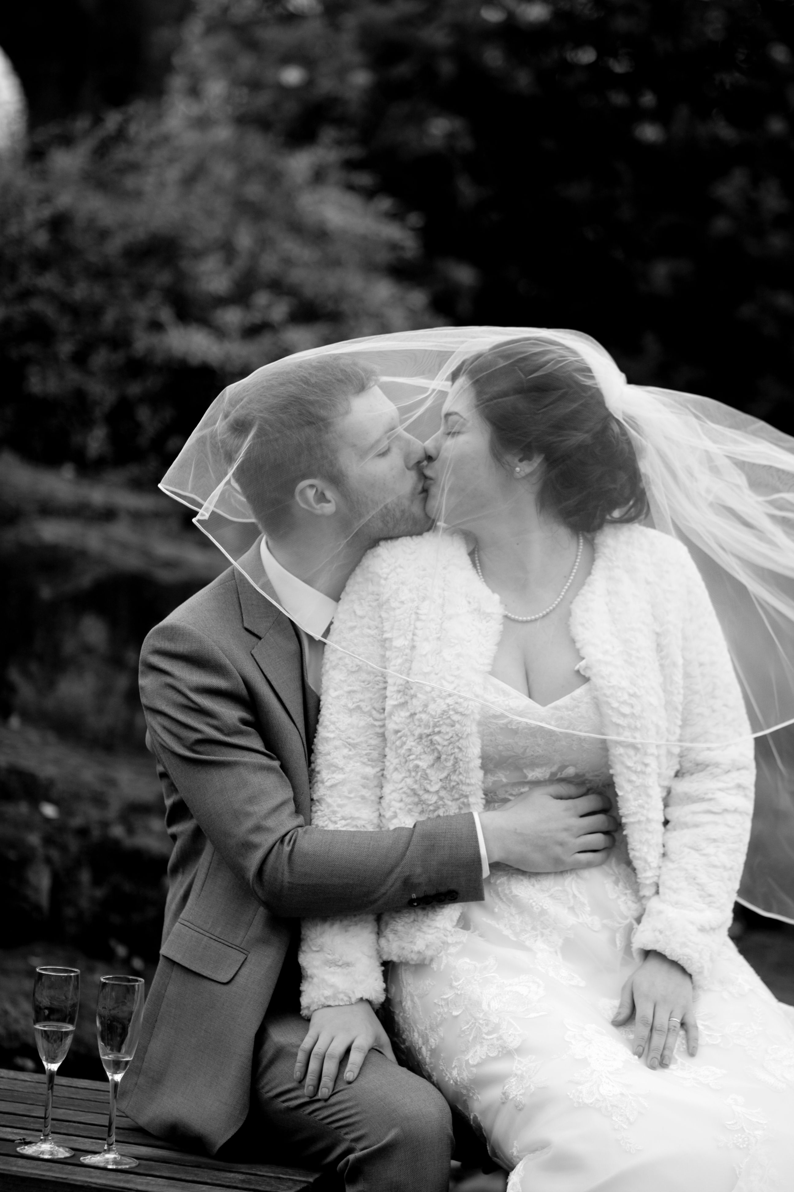 A couple shares a romantic kiss on their wedding day in an outdoor setting.