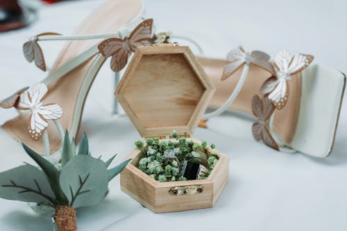 Composition of stylish wedding rings in creative wooden box placed on table near white trendy high heeled shoes