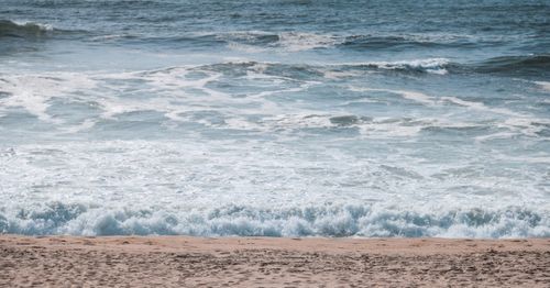 Free Gentle ocean waves meeting a sandy beach under clear skies, perfect for relaxation. Stock Photo