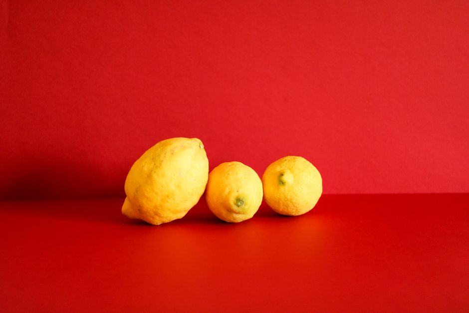 A trio of fresh yellow lemons on a vibrant red backdrop in a studio setting.