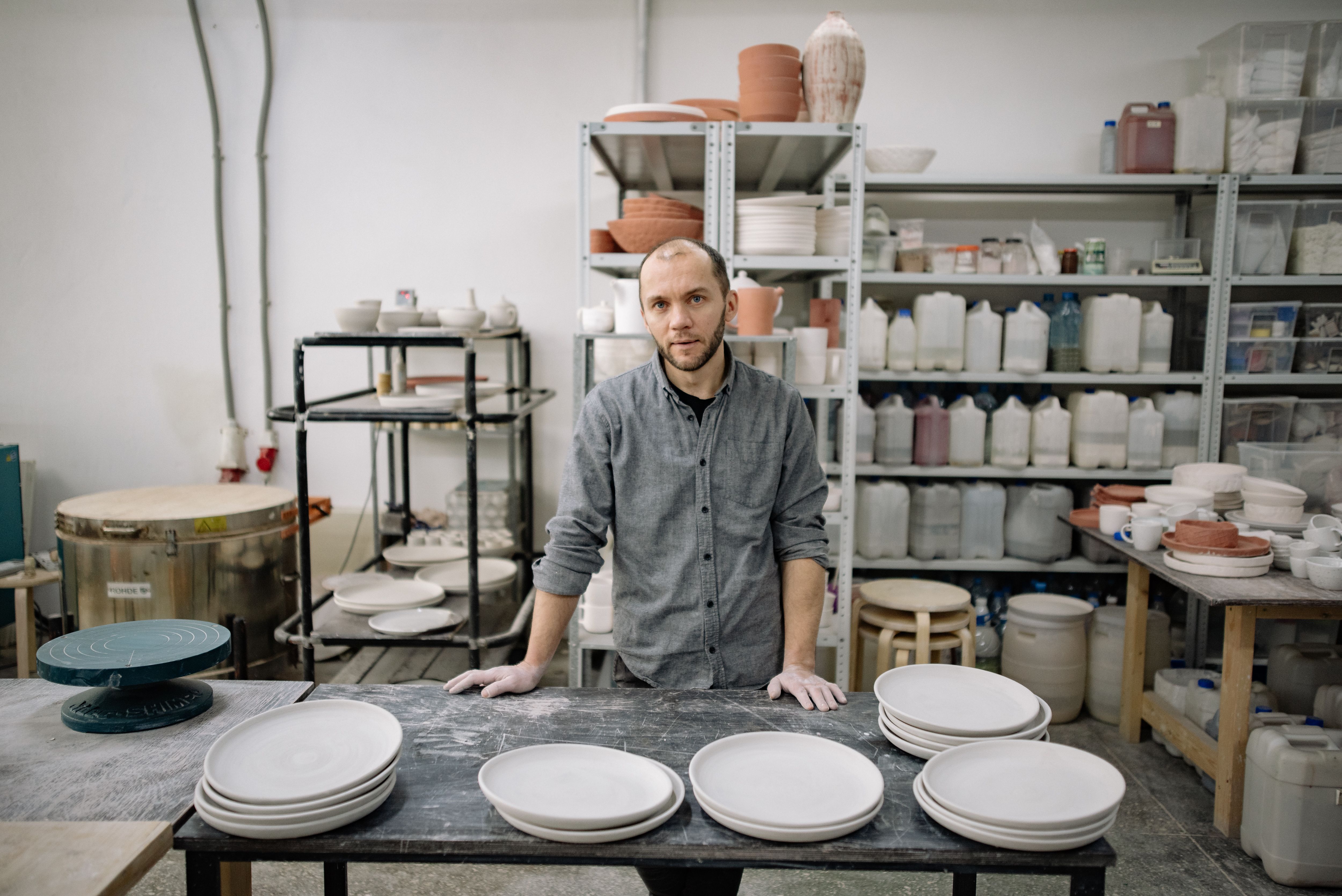 Man in a ceramics workshop standing by a table with plates and pottery materials.