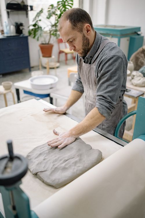 Free Adult male artisan shaping clay on a workbench in a creative studio setting. Stock Photo