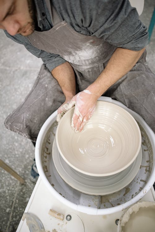 Royalty-Free photo: Person in gray shirt and gray pants molding clay pot