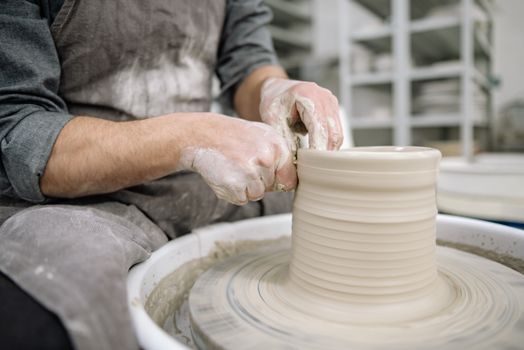 Potter shaping clay on a pottery wheel, showcasing artisan skill indoors.