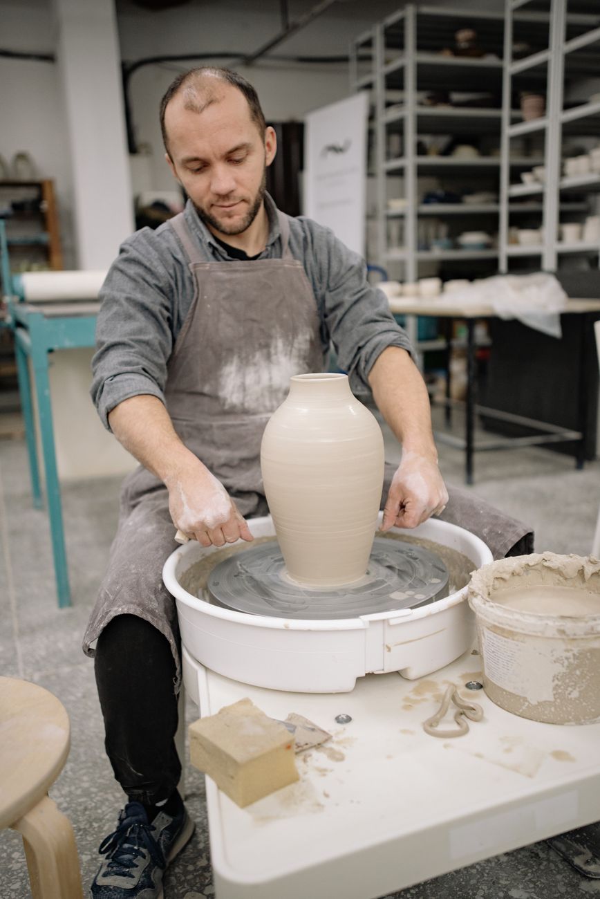 A dedicated artisan expertly molds a clay vase on a pottery wheel in a workshop setting.