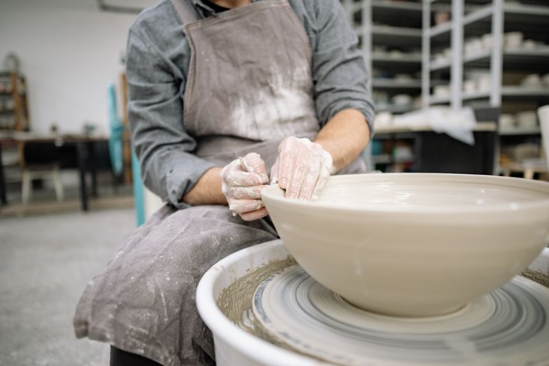 Artisan coiling a clay slab around a wooden rotating holder to form the cylindrical body of a Zisha teapot — the围身 technique