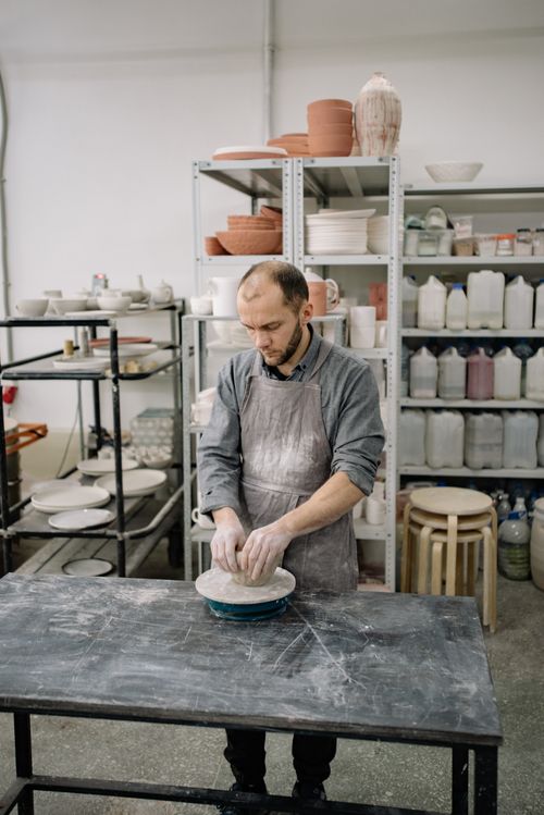Free Man shaping clay on a pottery wheel in a rustic indoor workshop. Stock Photo