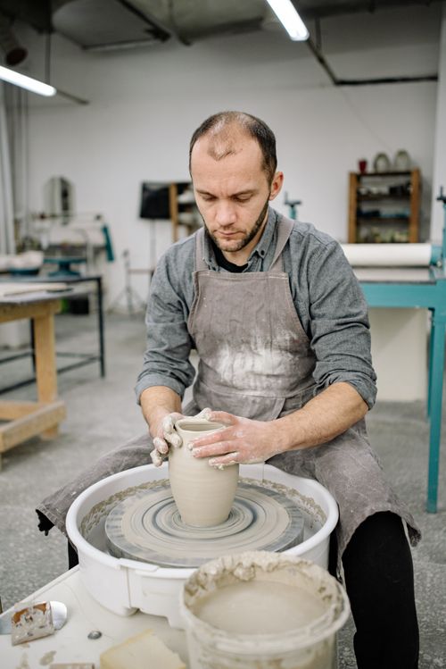 Free A man crafts pottery on a wheel in a workshop, focusing on creating a clay vase. Stock Photo