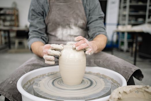 A skilled craftsman shapes pottery on a wheel indoors, showcasing artistry and skill.