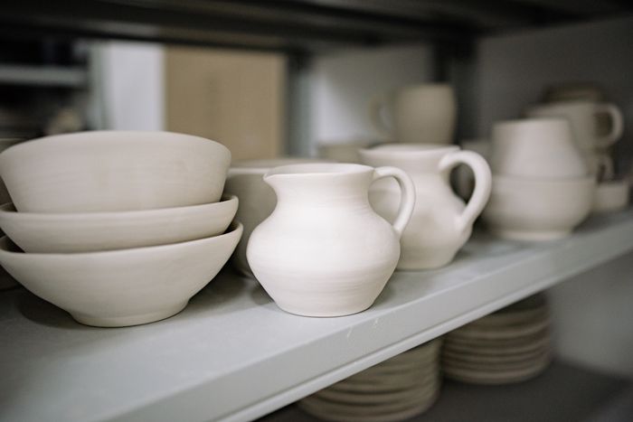Hand-thrown white stoneware pitchers and bowls on a studio shelf
