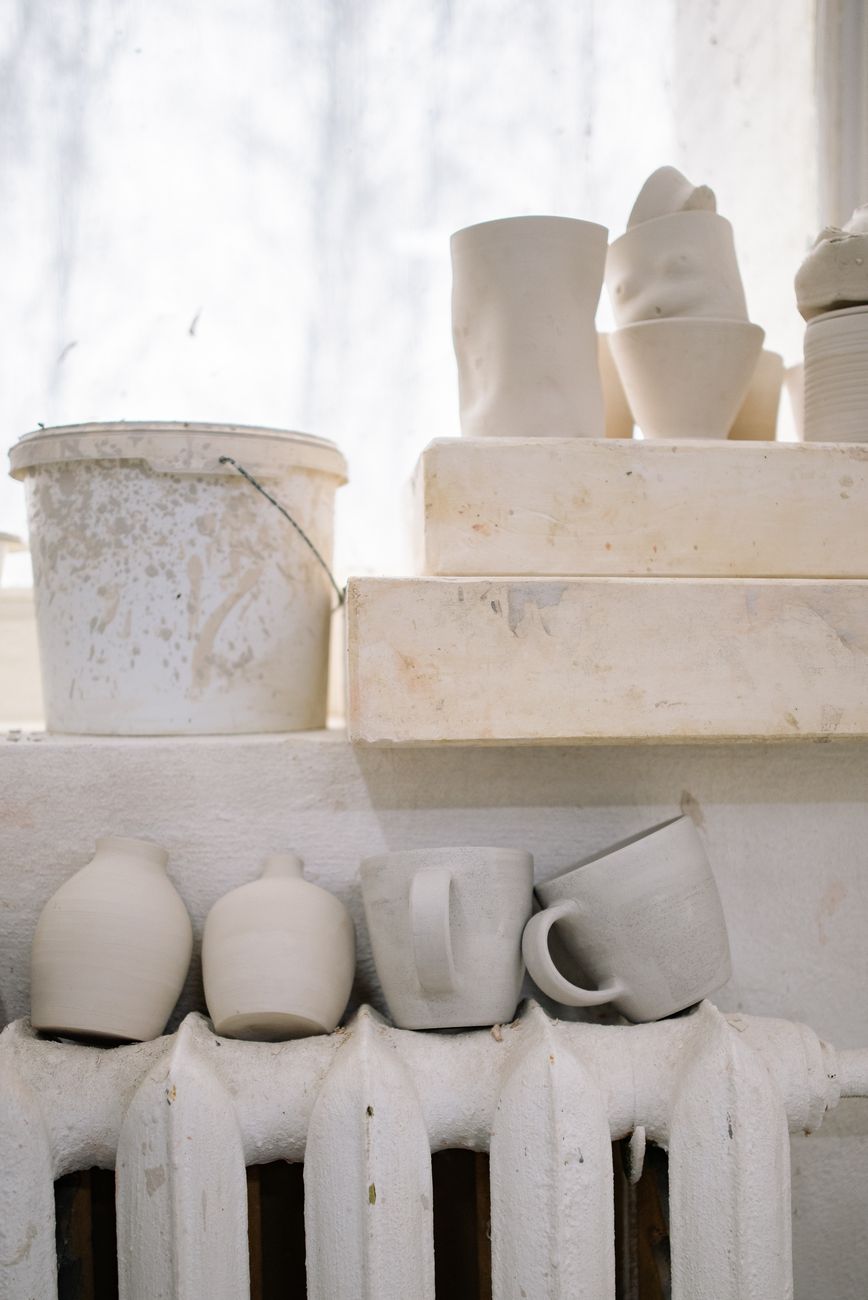 A close-up of raw ceramic cups and a bucket in a sunlit workshop, showcasing rustic pottery craft.