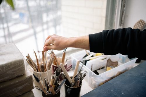 Free A hand reaching for pottery tools in an art studio, showcasing the craft of pottery making. Stock Photo