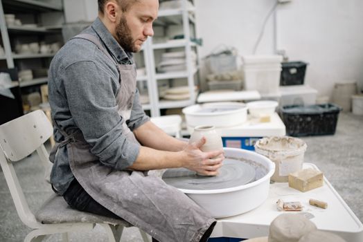 A focused man in a workshop crafting pottery on a wheel, showcasing skill and craftsmanship.