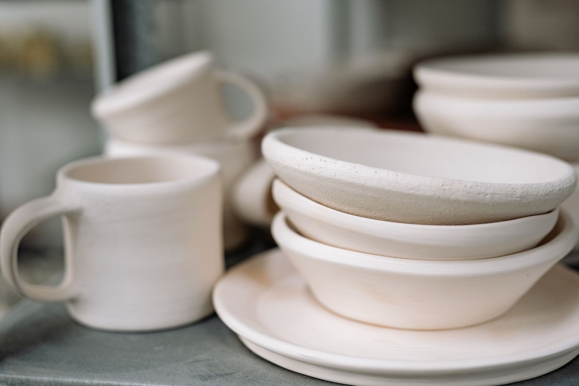 A close-up view of a handcrafted white ceramic dinnerware set including bowls, plates, and cups.