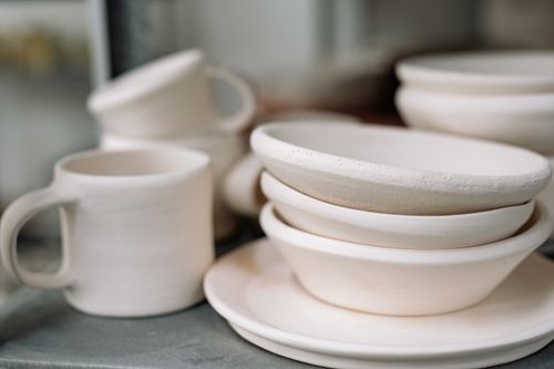 Free A close-up view of a handcrafted white ceramic dinnerware set including bowls, plates, and cups. Stock Photo