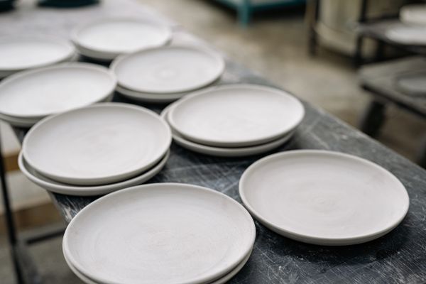 Stacked handcrafted stoneware plates on a workbench, photo by Yan Krukau on Pexels