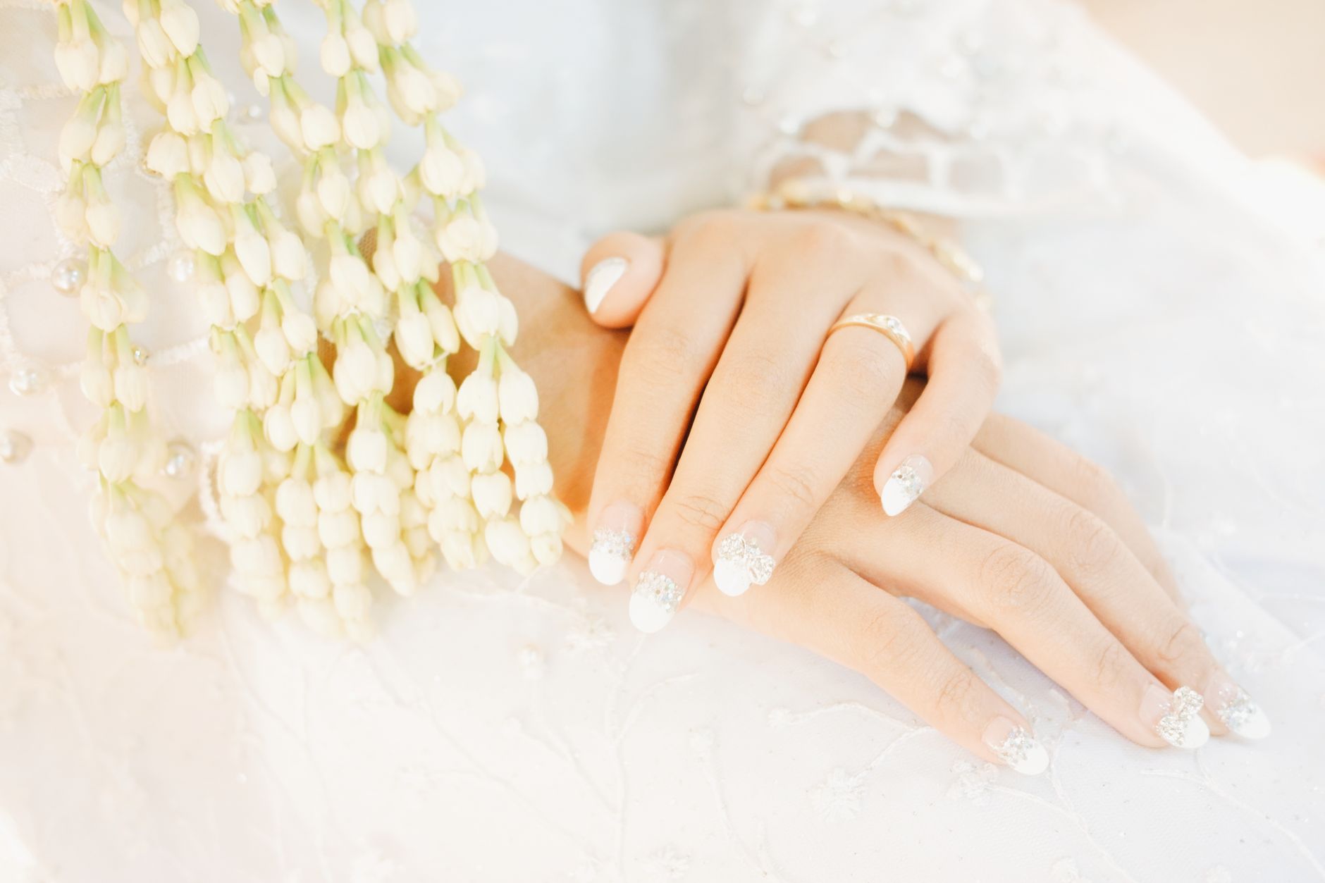 Close-up of a bride's hands with intricate manicure and floral decor, symbolizing elegance and celebration.