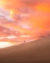 Anonymous traveler walking on sandy dune in endless desert against picturesque cloudy sunset sky