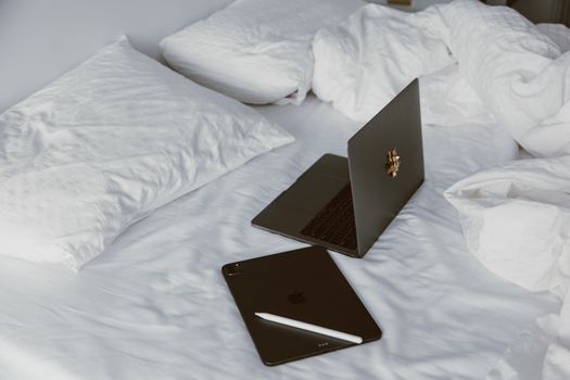 A modern home office setup with a laptop and tablet on a white bed, perfect for remote work or leisure.