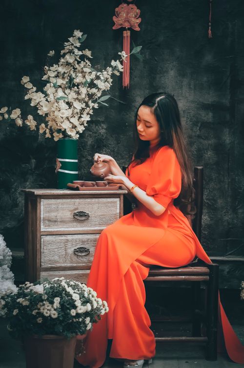 Free A woman in a red dress elegantly pours tea in an indoor setting with floral decor. Stock Photo