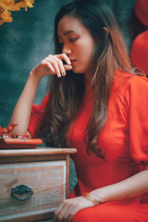 Free A thoughtful woman sits indoors in traditional red attire beside a wooden table. Stock Photo