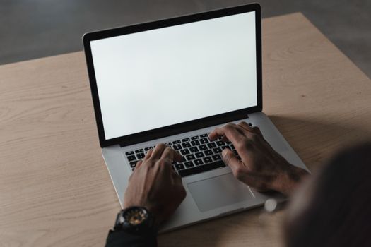A person typing on a laptop with a blank screen on a wooden desk, ideal for mockups.