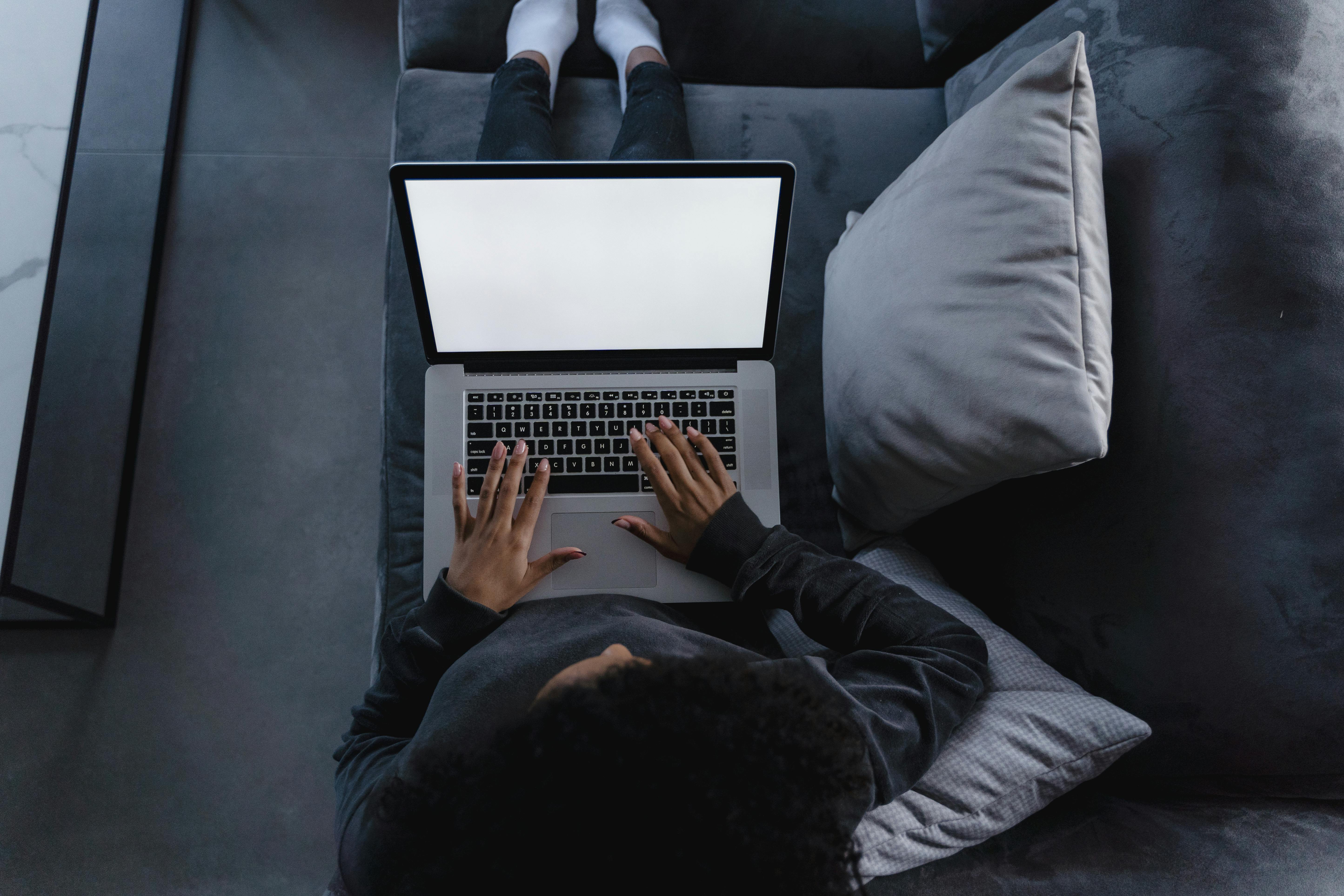 A person is using a laptop while sitting comfortably on a couch at home, viewed from above.