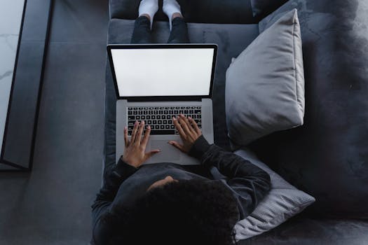 A person is using a laptop while sitting comfortably on a couch at home, viewed from above.