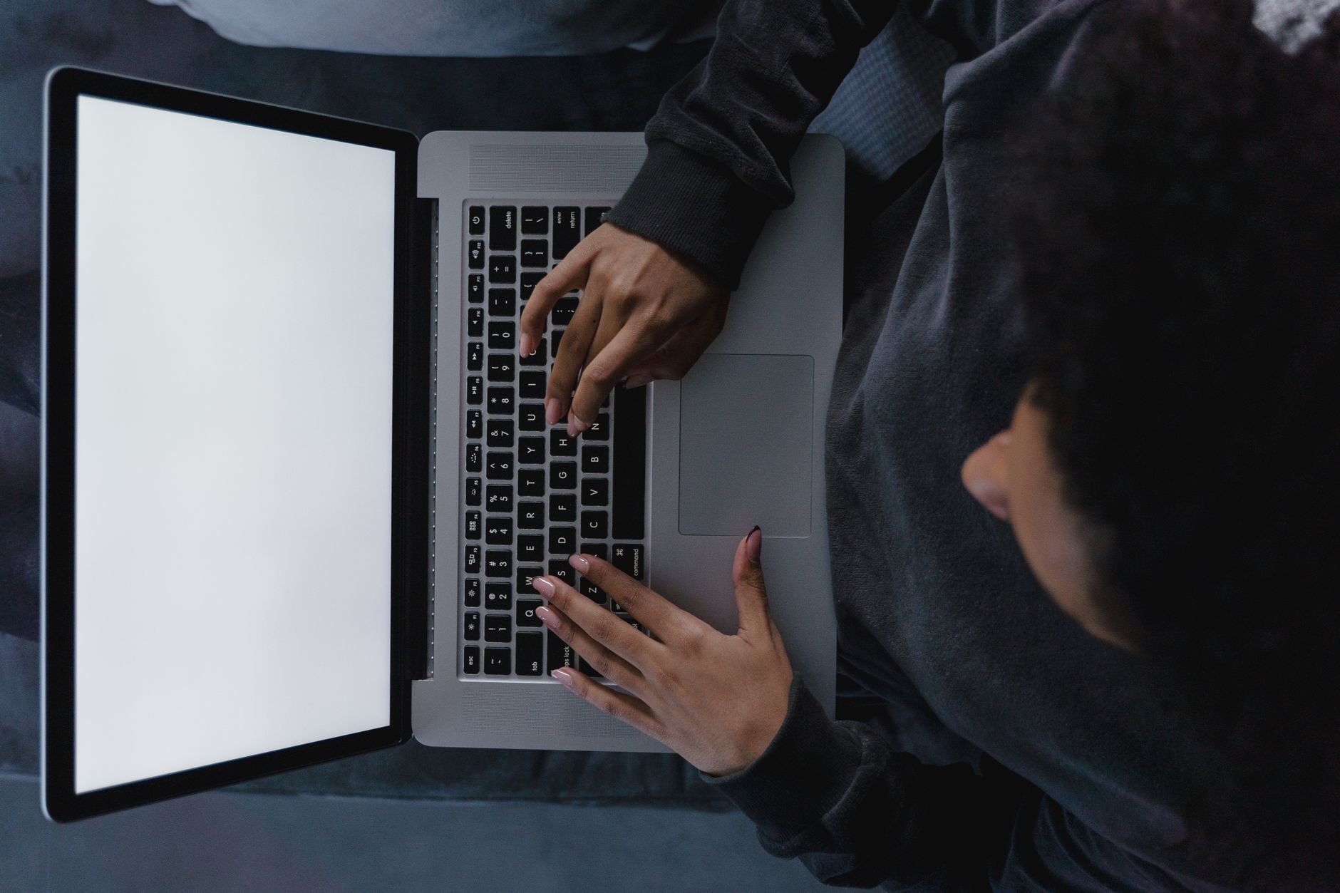 Overhead shot of a person working on a laptop with a blank screen in a dimly lit room.