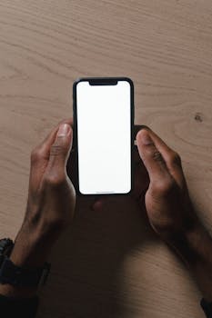 Close-up of hands holding a smartphone with a blank screen over a wooden surface.