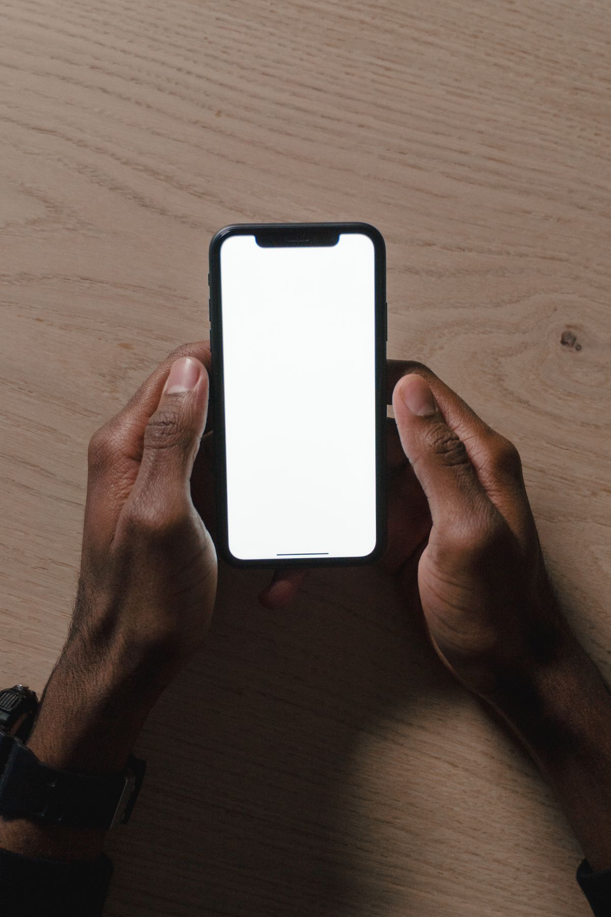Close-up of hands holding a smartphone with a blank screen over a wooden surface