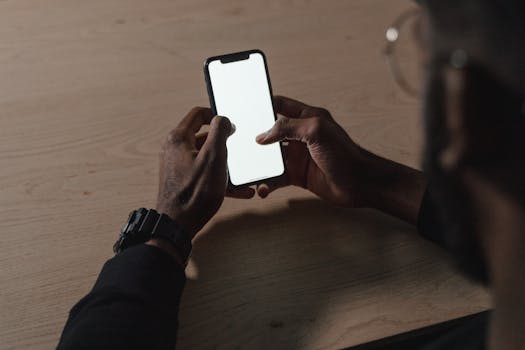 Close-up of hands holding a smartphone with a blank screen on a wooden desk.