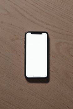 Vertical shot of a smartphone with a blank screen on a wooden surface, ideal for mockup use.