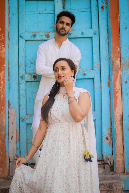 Free Young couple in traditional attire posed in front of a rustic blue door, showcasing style and culture. Stock Photo