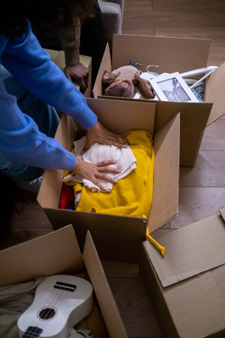 A Person Packing Clothes In A Cardboard Box